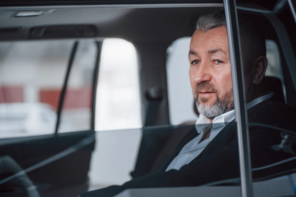 Break between trip. Senior businessman in official clothes sitting in a modern new car